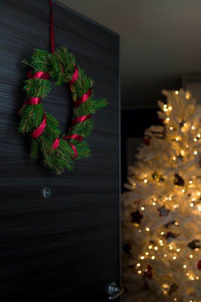 istock Fresh pine wreath on front door, opening on christmas tree. Vertical shot. 1290746236