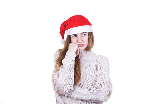 Studio shoot of young caucasian european woman thinking and looks upset in christmas with red santa hat isolated on white background, shot with canon 5DSR, 100 iso