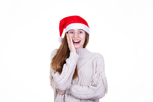 Studio shoot of young caucasian european woman looking surprised by the christmas gift with red santa hat isolated on white background, shot with canon 5DSR, 100 iso