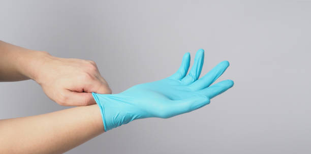 istock Left hand is pulling right hand wearing blue latex gloves on white background. 1290747382