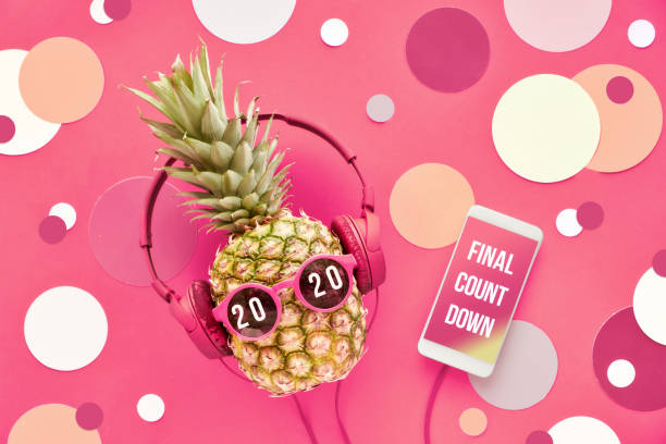 Pineapple in sunglasses and earphones with smart phone 2020 go away Final countdown for year 2020, Happy New Year 2021 Funny pineapple in sunglasses and pink earphones listening to music on smart phone. Flat lay on red paper background with circles.. its the final countdown stock pictures, royalty-free photos & images