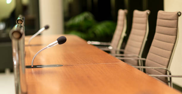 vista aislada de un micrófono en la parte delantera de una sala de conferencias entre otros micrófonos borrosos en el fondo - diplomacy fotografías e imágenes de stock