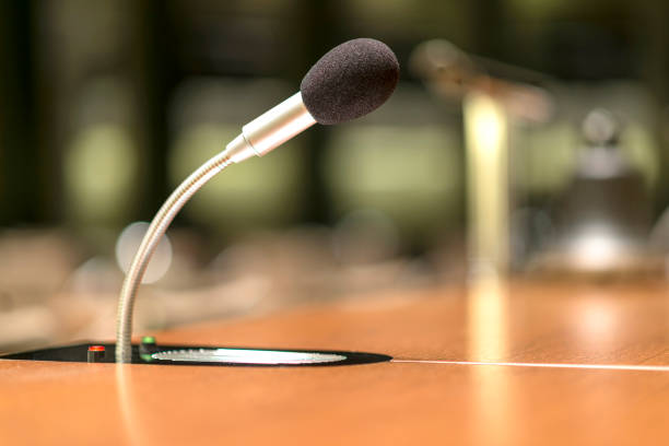 vue d’isolement d’un microphone à l’avant d’une salle de conférence parmi d’autres mikes brouillés à l’arrière-plan - press conference microphone seminar table photos et images de collection