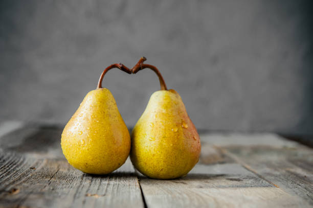 un paio di pere gialle organiche mature gialle fresche formano la forma del cuore su un tavolo rustico in legno sullo sfondo in pietra grigia. relazioni, concetto d'amore. colori di tendenza dell'anno 2021. copiare lo spazio. - two pears foto e immagini stock