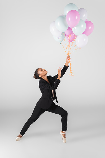 african american businesswoman performing ballet with balloons isolated on grey