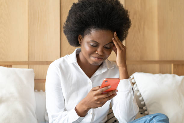 istock Frustrated Woman Using Smart Phone While Sitting On Bed At Home 1290757580