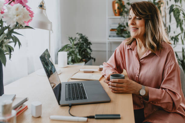 istock Happy Senior Woman Sitting in her Home Office and Using her Laptop Computer while Drinking Coffee 1290760650