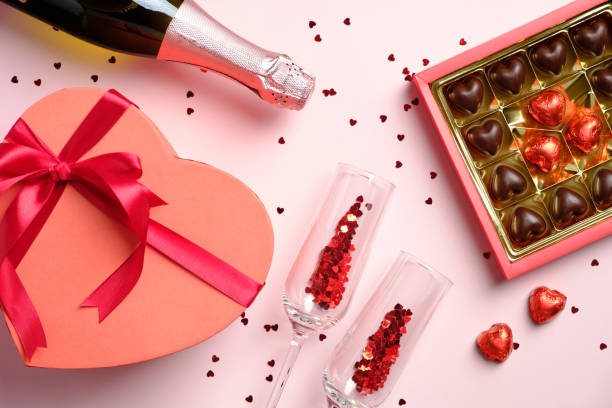 istock Happy Valentines day celebration concept. Flat lay composition with heart shaped box decorated red ribbon bow, sweets, wine and glasses on pink table. Top view. 1290760856
