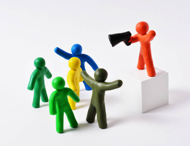 istock Plasticine figures of people gathered in a group near a white cube with an orator, the orator speaks in megaphone, the concept of rallies, protests, announcements 1290761011