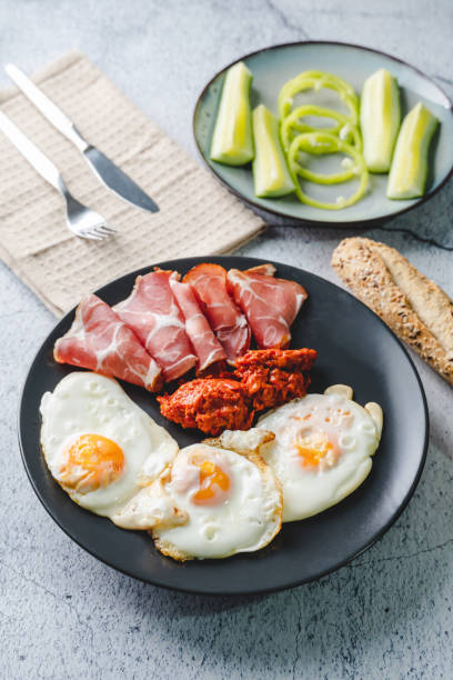 istock Top angle view on sunny side up eggs prosciutto coppa Capocollo dry meat and homemade ajvar paprika salad on the table as dinner or breakfast meal 1290766417