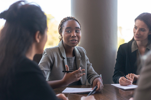 A confident black woman leads a meeting with a team of employees in an office boardroom.