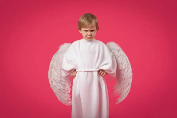 God Angel gets angry and punishes with glance. Child boy kid in suit with wings on pink solid background. Valentine day 14 february sins and holidays postcard concept.