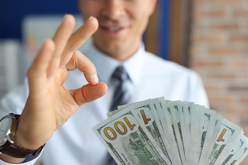 Man with dollar bills shows ok. Profit from business idea concept.
