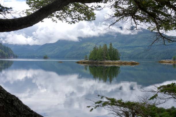 istock Tiny islands in flat calm sea with mountains and bright clouds with reflections tranquil scene wilderness 1290775426