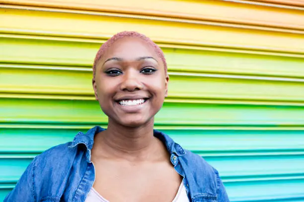 Happy teen smiles outdoors while standing by rainbow-colored wall
