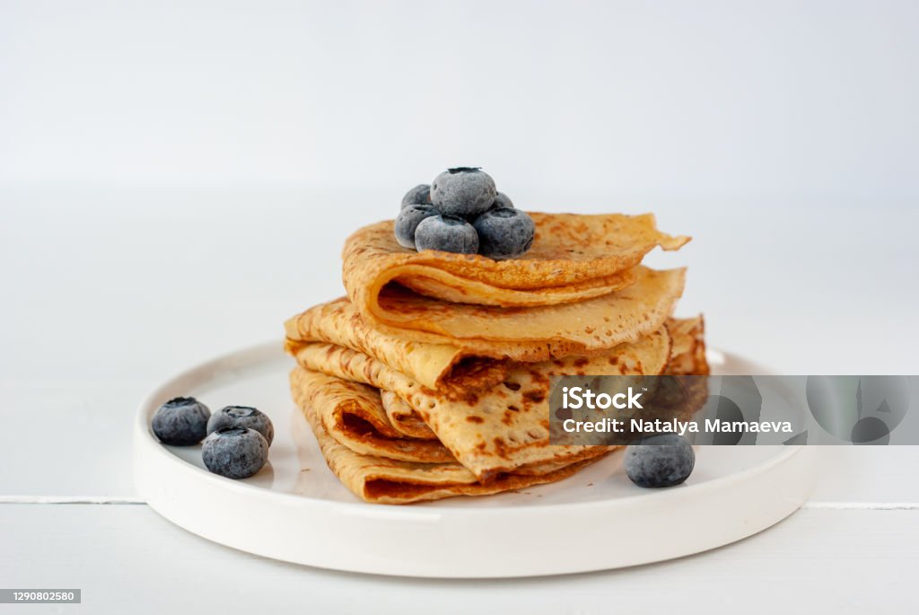 Vegan crepes with frozen blueberries Vegan crepes made from chickpea flour, al purpose gluten free flour and oat milk, with frozen blueberries on a white wooden table Crêpe - Pancake Stock Photo