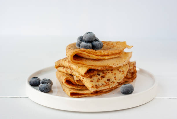 Vegan crepes with frozen blueberries Vegan crepes made from chickpea flour, al purpose gluten free flour and oat milk, with frozen blueberries on a white wooden table crêpe pancake photos stock pictures, royalty-free photos & images