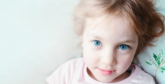 Beautiful child with big eyes is lying on pillow in the bedroom