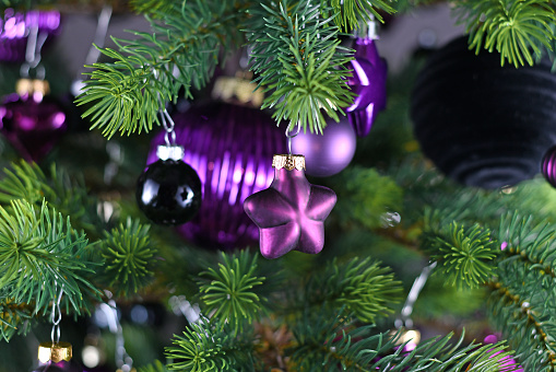 Close up of star shaped purple glass tree ornament bauble with decorated Christmas tree with other seasonal tree ornaments in background