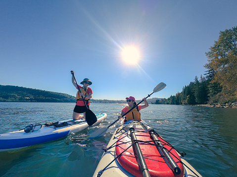 istock Hermanas multiétnicas remando en Stand Up Paddleboard y en Kayak 1290813023