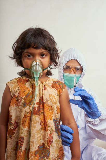 Virologist in protective suit makes vaccination to Little girl patient infected with Corona Virus stock photo