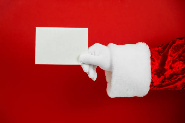 istock Santa Claus hand holding empty Christmas card. Mock up blank sign 1290816971