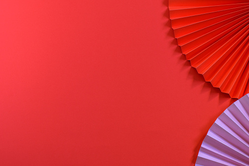 Red background with trendy eco friendly red and pink chinese paper fans. Nice design for greeting card, or party invitation or any design purposes. Mock up photo, top view.
