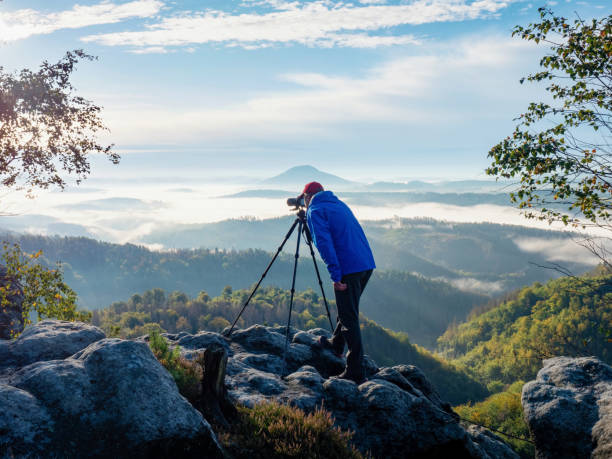 fotograf rahmt szene im sucher ein. kamera auf stativ zum fotografieren von nebligen landschaften - behind photographer men mountain climbing stock-fotos und bilder