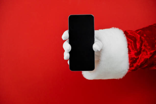 Santa Claus hand holding a smartphone with a blank screen. Mobile phone during holiday time, mockup stock photo
