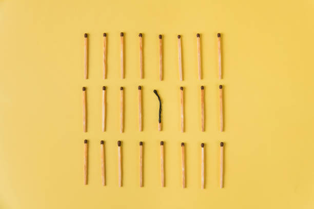 one burnt match among many other matches. Top view on isolated yellow background.