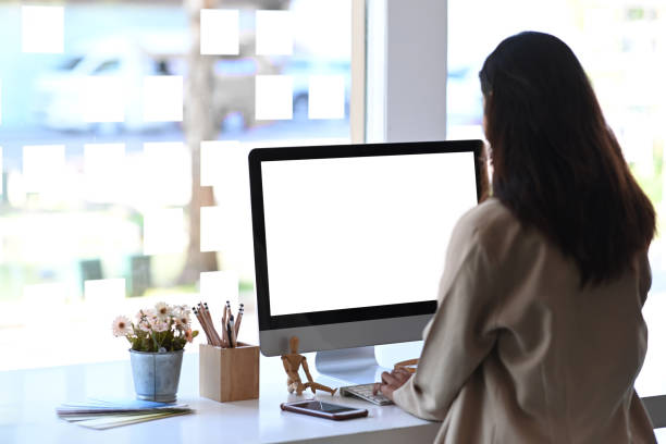 istock Rear view of young female employee working on computer in modern office. Blank screen for product montage. 1290827476