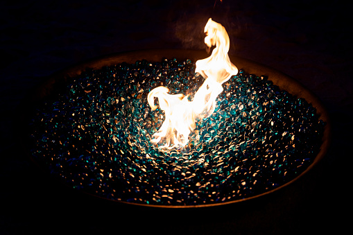Glowing blue glass rocks in outdoor, close up outdoor fireplace with a flame.