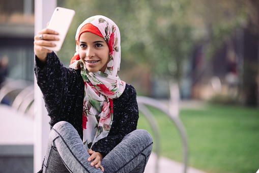 Teenage girl shoot a selfie on mobile phone while in the city park waiting for her friends.