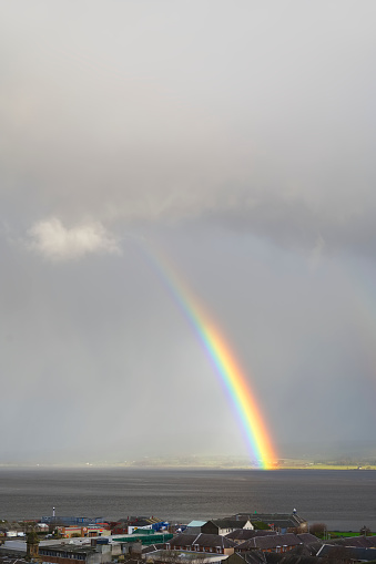 Bright rainbow high in sky over the sea during dark storm uk