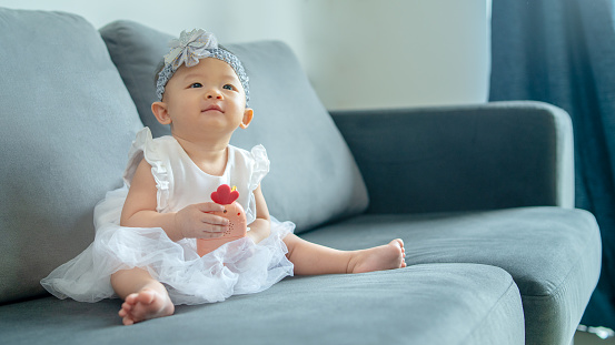 Asian newborn baby girl smiling and looking away. She is sitting on the sofa in the living room.