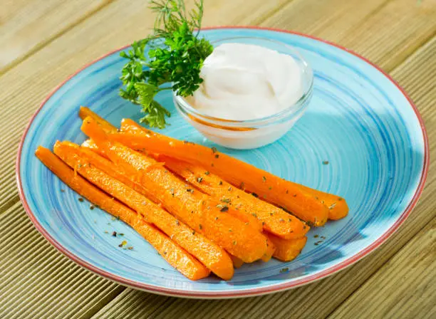 Healthy eating concept. Boiled carrot sticks served with creamy dip and greens