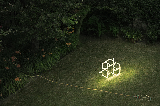 Neon-tube recycling symbol in a garden. *** The symbol is a digital render and a release is provided ***