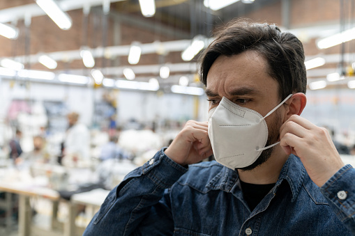 Portrait of a Latin American man working textile factory during the COVID-19 pandemic and fixing his facemask