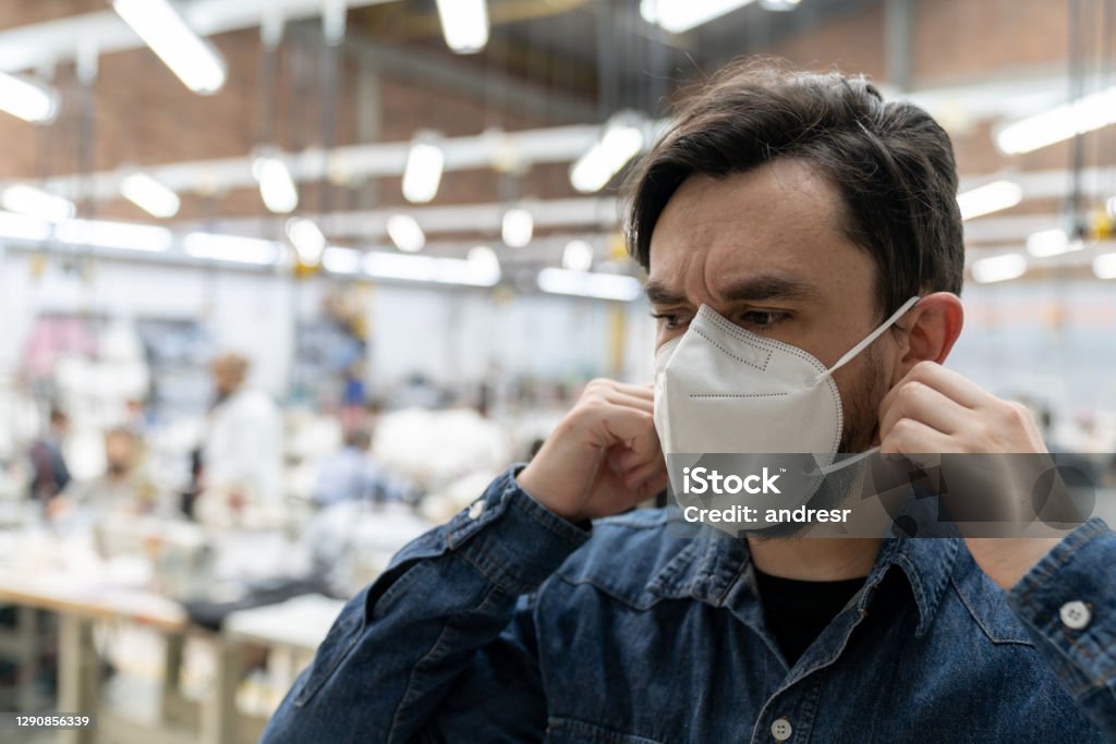 Man working textile factory during the COVID-19 pandemic and fixing his facemask Portrait of a Latin American man working textile factory during the COVID-19 pandemic and fixing his facemask N95 Face Mask Stock Photo