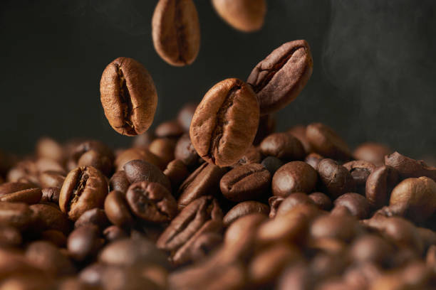 Close up of roasted coffee beans on a black smokey background. Close up of roasted coffee beans on a black smokey background. The grains fall from above in a group. coffee crop stock pictures, royalty-free photos & images