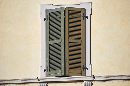 Italian classic window on the bright wall facade with closed wooden green shutters