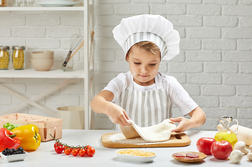 little child boy in cap and an apron cooking pizza in the kitchen