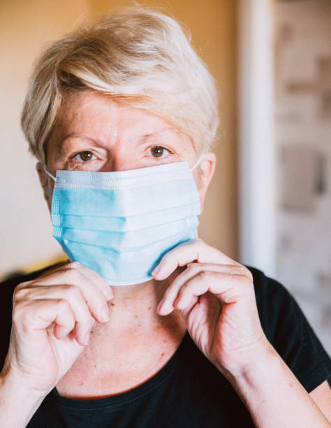 istock Senior woman putting on a protective face mask 1290870338