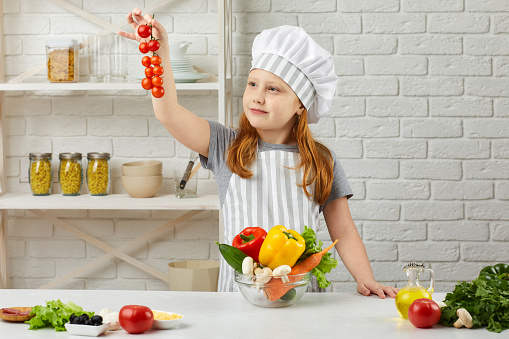 little child girl in chef hat and an apron holding bowl of fresh vegetables