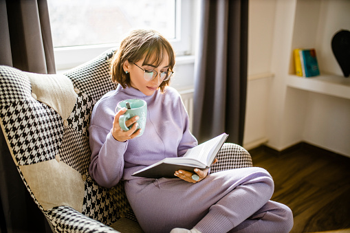 Beautiful young woman relaxing with book and coffee at home
