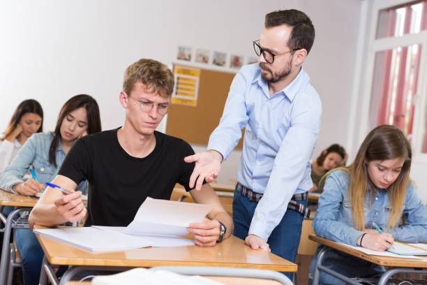 istock Schoolboy is writing answer the question on paper and teacher explaining it 1290874468