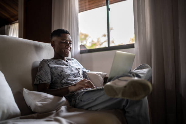 istock Young man using laptop sitting on the couch at home 1290876467