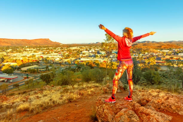 Carefree woman looking at panoramic view of Alice Springs at sunset and surrounding ranges from Anzac Hill at 608 meters. Northern Territory, Central Australia. Famous lookout over the city of desert.
