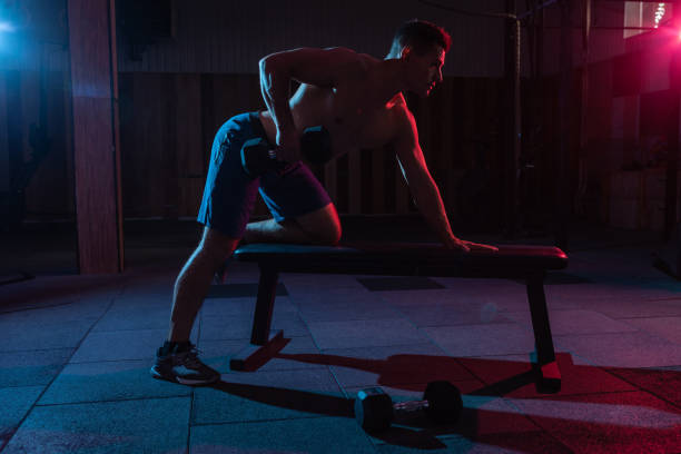 istock Muscular man exercise with dumbbell in red-blue gradient light in dark gym hall 1290882968