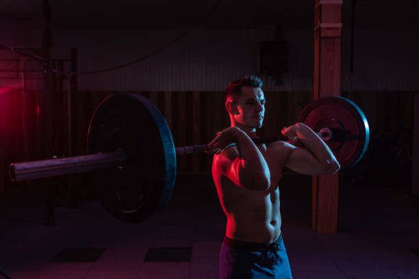 istock Working out by lifting weights in dark cross-training gym. Muscular powerful man with heavy barbell in red blue neon light 1290883109